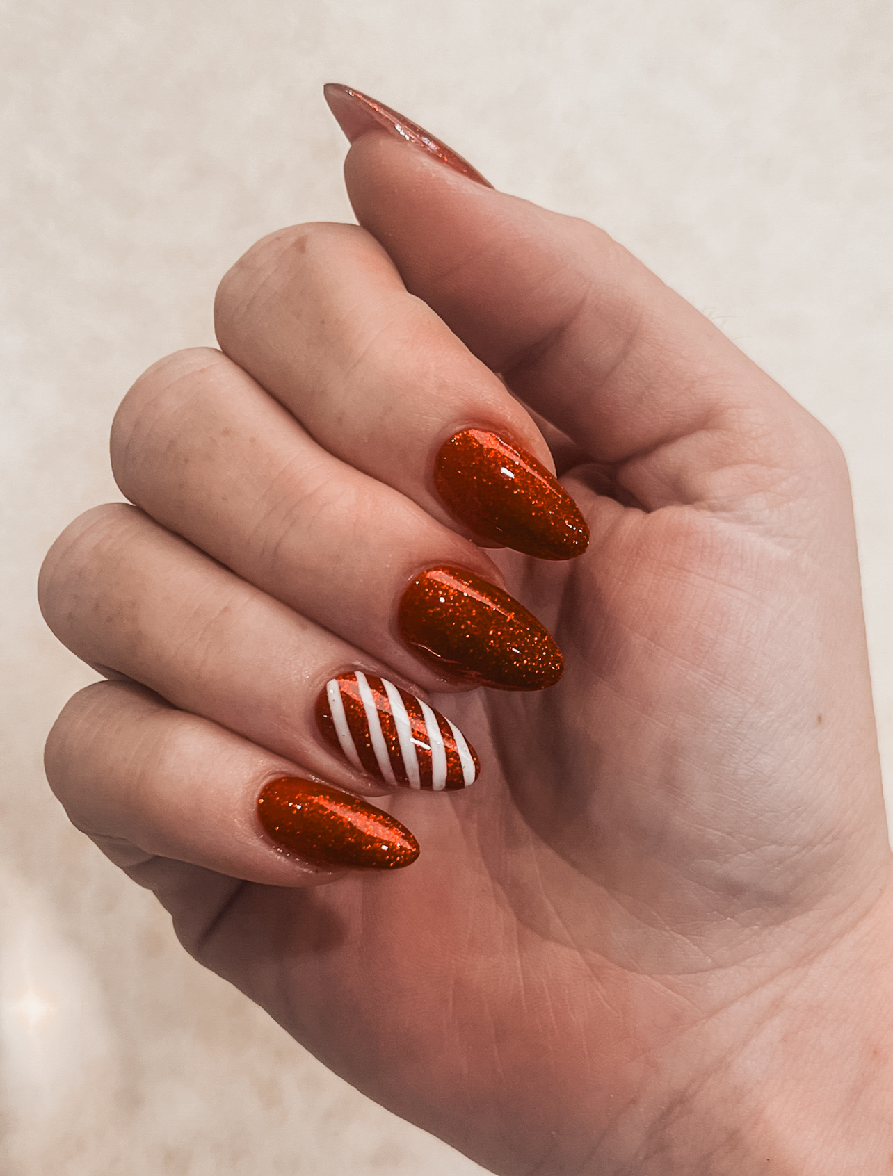 Glittery red almond nails with a striped accent nail